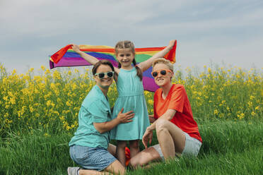 Happy lesbian mothers with daughter holding rainbow flag - VSNF00970