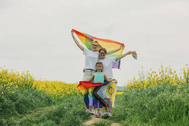 Happy lesbian mothers standing with daughter and holding rainbow flag at field - VSNF00983