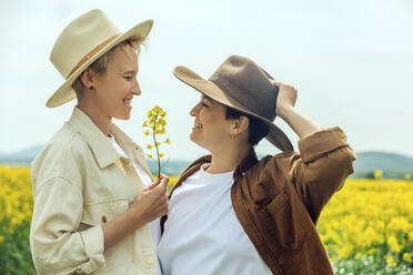 Happy lesbian couple wearing cowboy hat at field - VSNF00991