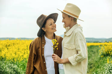 Happy lesbian couple wearing cowboy hat standing at field - VSNF00992