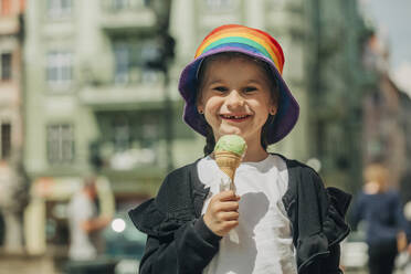 Lächelndes Mädchen mit buntem Eimer Hut hält Eis - VSNF00993