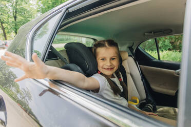 Glückliches Mädchen mit winkender Hand im Auto sitzend - VSNF01008