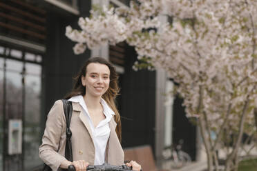 Happy businesswoman standing in front of cherry blossom flower tree - VIVF01046