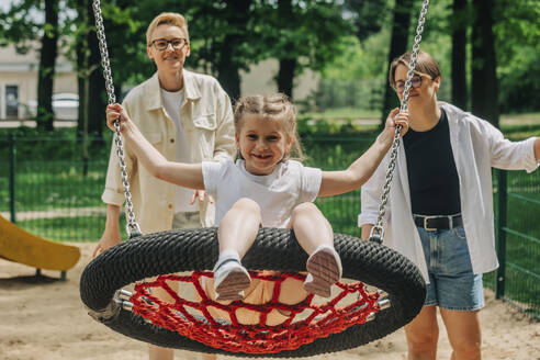 Lesbische Mütter mit Tochter schwingen Schaukel auf Spielplatz - VSNF01009