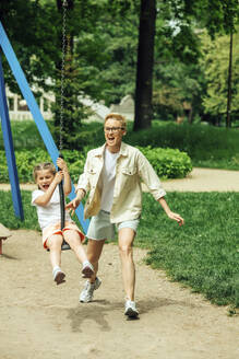 Fröhliche Mutter mit Tochter, die auf dem Spielplatz schaukelt - VSNF01014