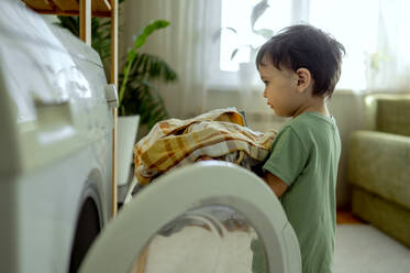 Junge mit Kleidung vor der Waschmaschine zu Hause stehend - ANAF01493