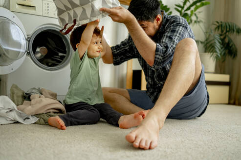 Glücklicher Vater und Sohn haben Spaß mit Wäschekorb und Wäsche waschen in der Maschine zu Hause - ANAF01497