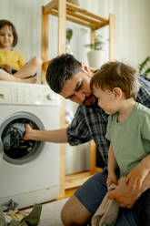 Father and son washing clothes in machine at home - ANAF01498