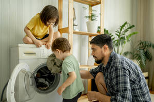Vater mit Kindern hilft beim Waschen der Wäsche in der Maschine zu Hause - ANAF01499