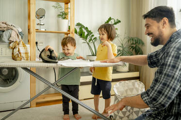 Happy children helping father ironing clothes at home - ANAF01504