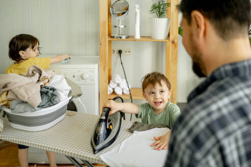 Vater mit Sohn beim Bügeln von Kleidung zu Hause - ANAF01505