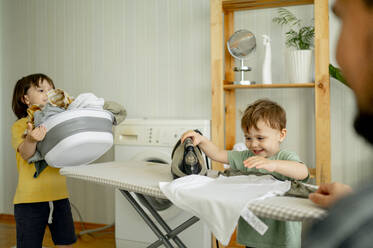 Lächelnder Junge beim Bügeln von Kleidung mit seinem Bruder zu Hause - ANAF01506