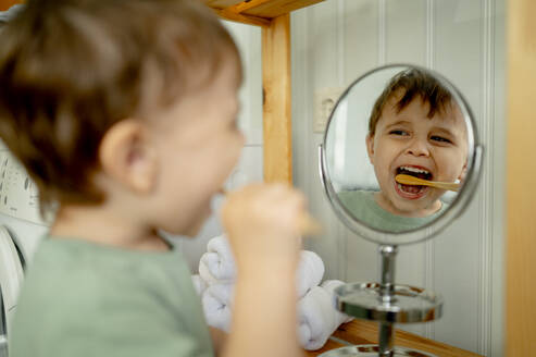 Boy brushing teeth looking in mirror at home - ANAF01510