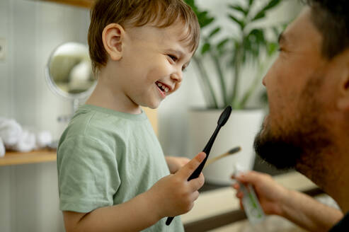 Happy man with boy holding toothbrush at home - ANAF01511