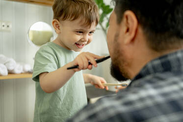 Happy boy brushing teeth of father at home - ANAF01512