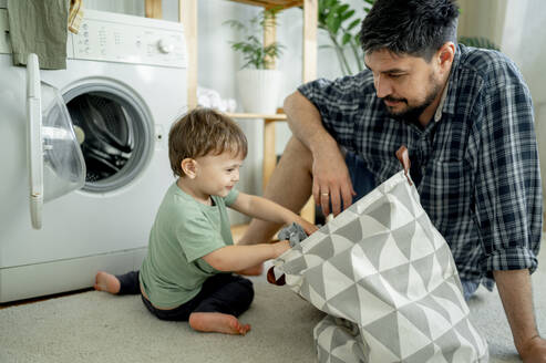 Junge hilft Vater beim Waschen der Wäsche in der Maschine zu Hause - ANAF01515