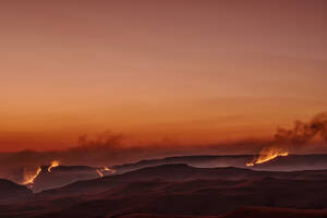 Brennende Savanne mit orangefarbenem Himmel im Hintergrund bei Sonnenuntergang, KwaZulu-Natal, Drakensberge, Südafrika - ANSF00407