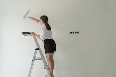 Girl standing on ladder and painting wall at home - OSF01591