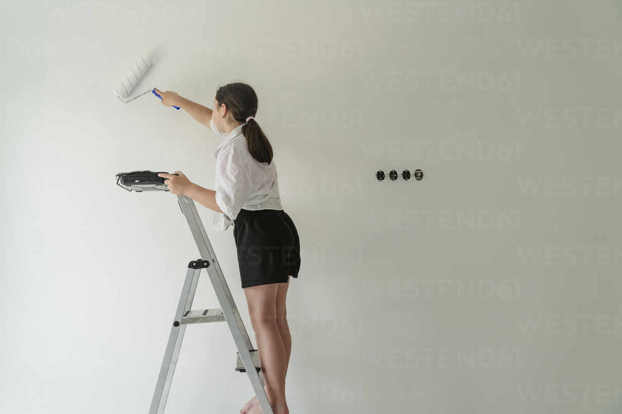 Germany, Cologne, Mature woman balancing on ladder during painting