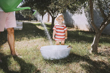 Ein kleiner Junge steht mit seinem Vater in einer Badewanne im Hinterhof und gießt Wasser - NDEF00720