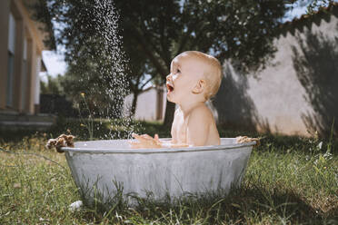 Kleiner Junge betrachtet das Wasser in der Badewanne im Hinterhof - NDEF00723