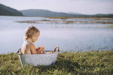 Verspieltes Mädchen spielt mit Blumen in der Badewanne am See - NDEF00728