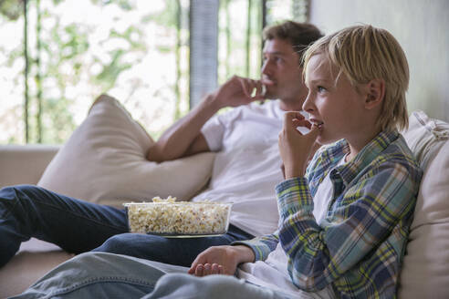 Vater mit Sohn isst Popcorn und sieht zu Hause fern - IKF00719