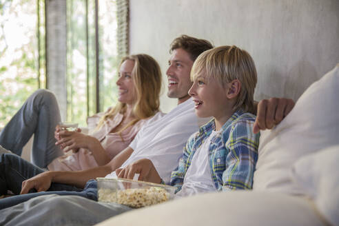 Happy mother and father with son watching TV at home - IKF00721
