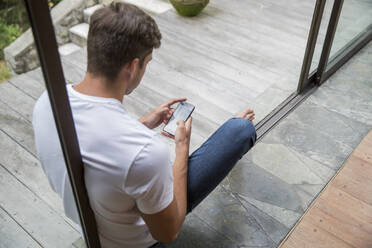 Young man using smart phone at home - IKF00729