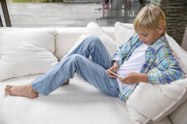 Smiling boy using smart phone on sofa at home - IKF00730
