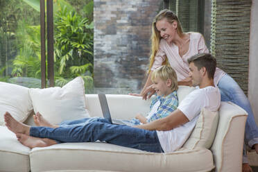 Happy man and woman with son using laptop at home - IKF00744