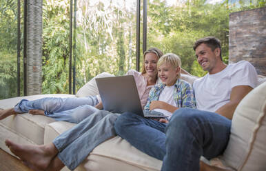 Happy father and mother with son using laptop in living room at home - IKF00747