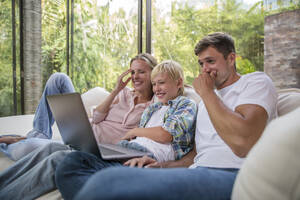 Glücklicher Vater und Mutter mit Sohn, die einen Laptop auf dem Sofa im Wohnzimmer zu Hause benutzen - IKF00748