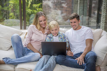 Glückliche Eltern mit Sohn, der zu Hause einen Laptop benutzt - IKF00749