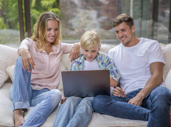 Glückliche Eltern mit ihrem Sohn, der einen Laptop im Wohnzimmer zu Hause benutzt - IKF00750