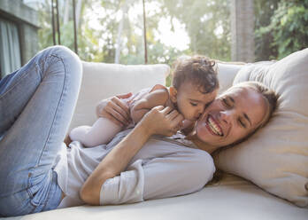 Happy mother having fun with daughter on sofa in living room at home - IKF00760