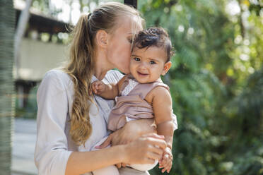 Mother embracing and kissing cute baby daughter - IKF00766