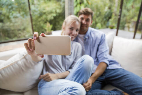 Happy couple taking selfie through smart phone at home - IKF00773