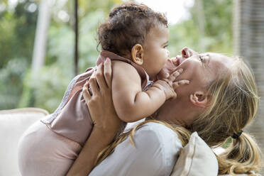 Cheerful mother with baby daughter embracing each other at home - IKF00775