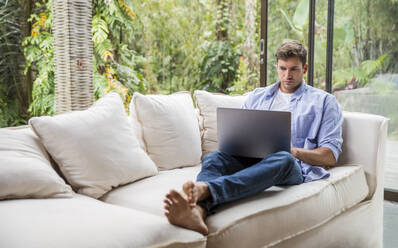 Young freelancer working on laptop at home - IKF00776