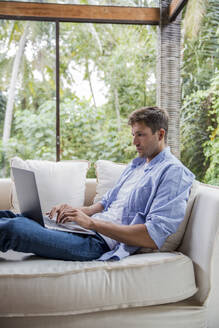 Freiberufler mit Laptop auf dem Sofa zu Hause - IKF00777