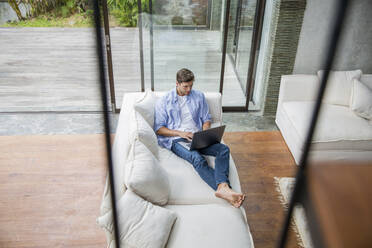 Freelancer working on laptop in living room at home - IKF00781