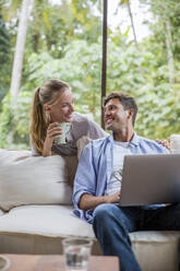 Happy freelancer with woman holding coffee cup at home - IKF00790