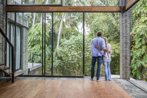 Loving couple standing by glass door at home - IKF00796