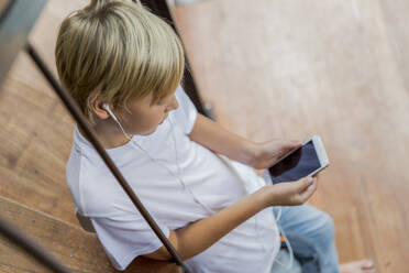 Boy wearing in-ear headphones using smart phone at home - IKF00811