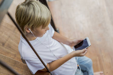 Junge trägt In-Ear-Kopfhörer und benutzt zu Hause sein Smartphone - IKF00811