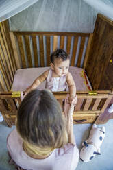 Mother with baby daughter playing in crib at home - IKF00815