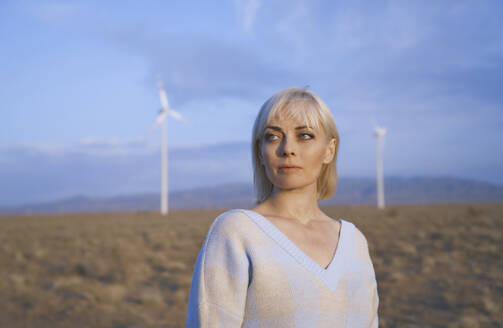 Blonde Frau steht in der Nähe von Windrädern in der Wüste - AZF00534