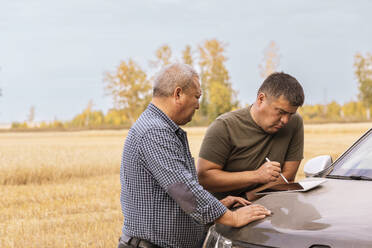 Man using tablet PC on car hood with father in wheat farm - ADF00109