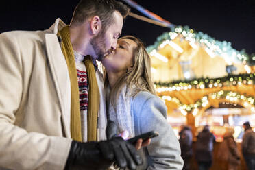 Junge Frau küsst Mann auf dem Weihnachtsmarkt - WPEF07357